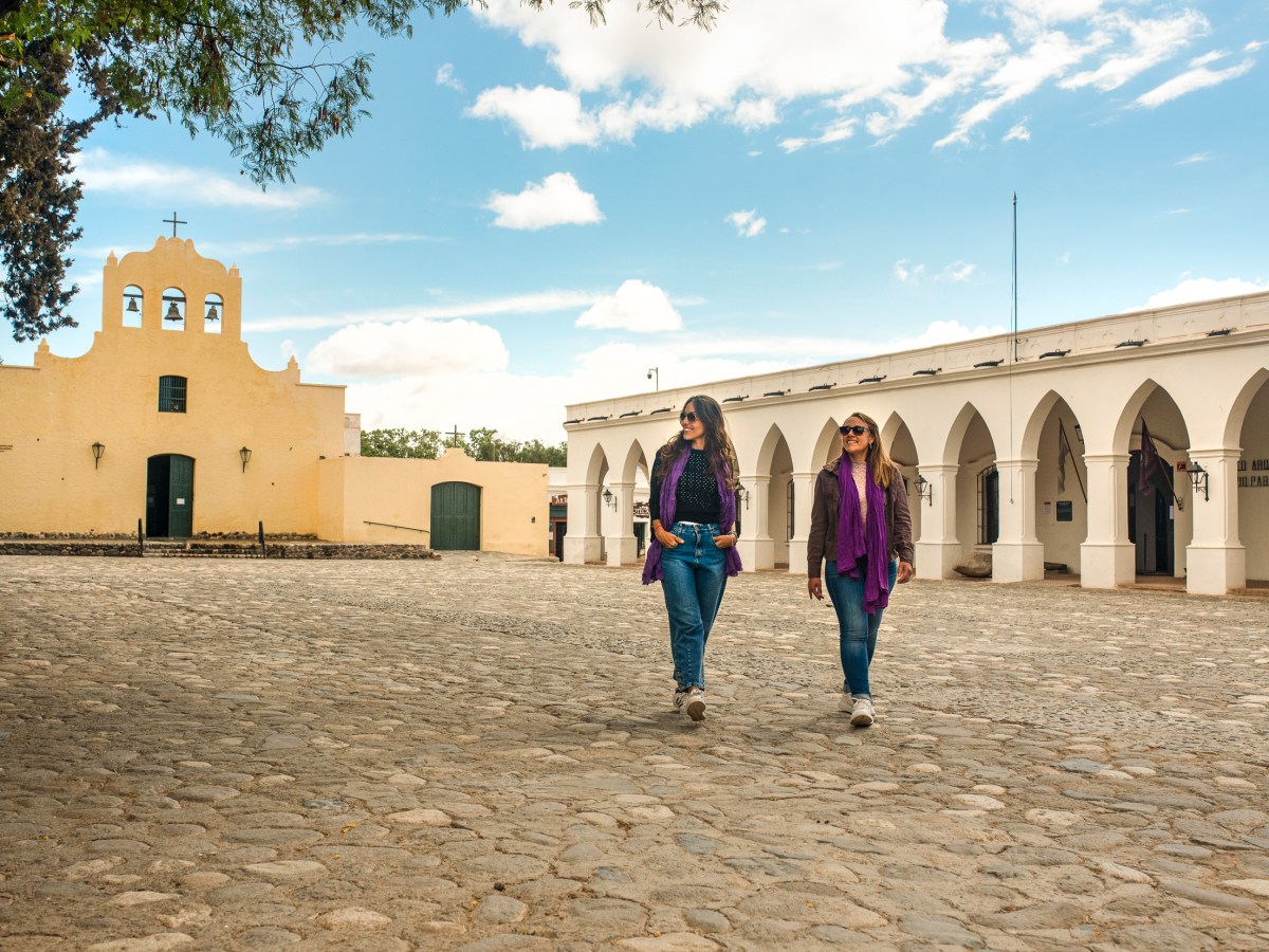 Capítulo: exploradoras caminhando em praça histórica com arquitetura colonial em viagem pelo Brasil.
